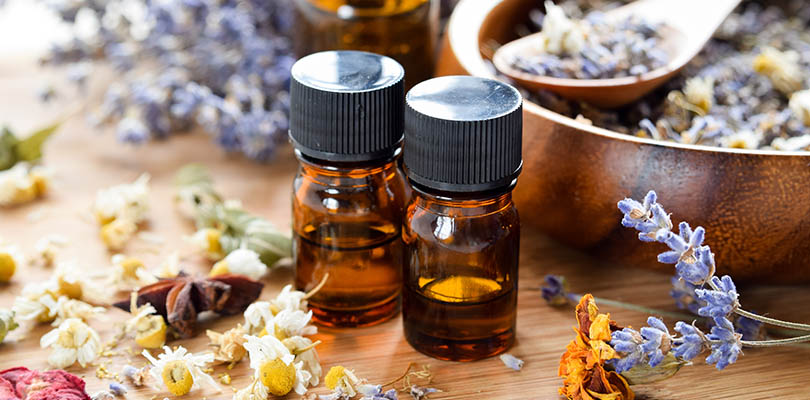 Two bottles of essential oils for cancer sit on a table with dried herbs